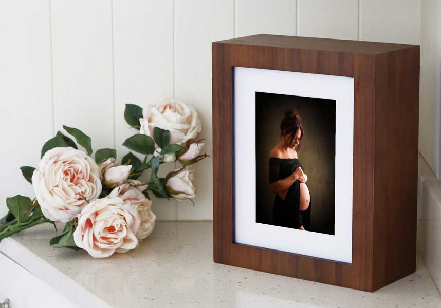 A framed photo of a pregnant person, part of their cherished Baby Plan, stands on a surface next to a bouquet of white roses.