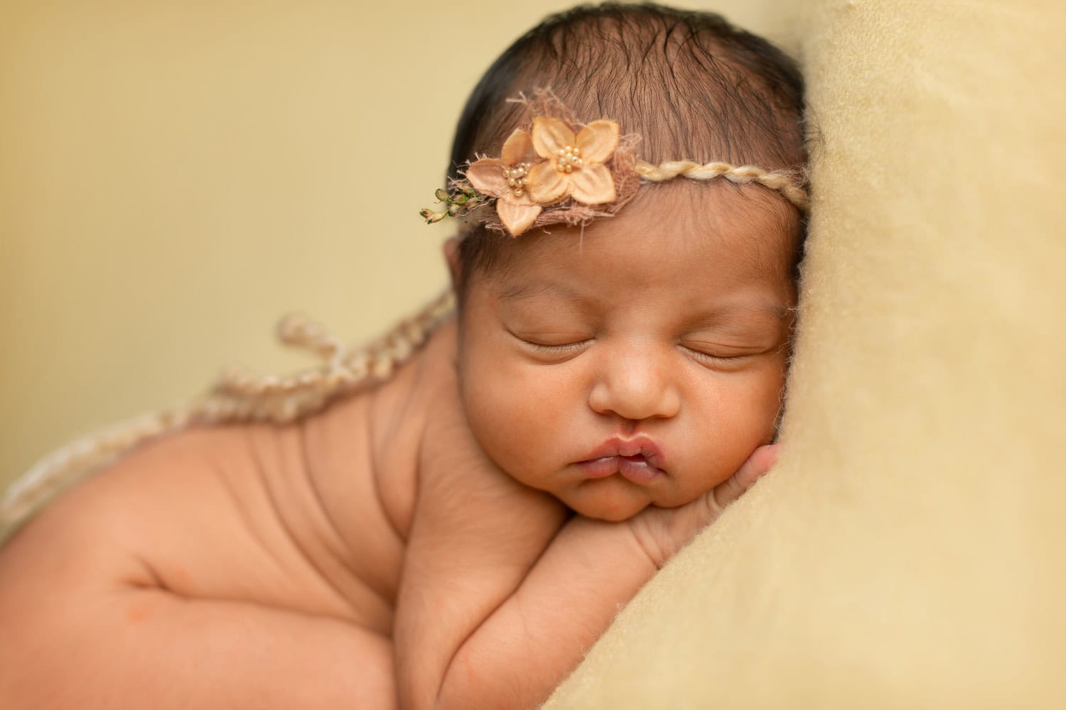 A newborn, adorned with a delicate floral headband, rests peacefully on a soft yellow surface.